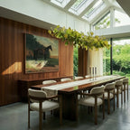 Clérachic's chandelier in its linear form, green glass leaves glowing above a dining table under skylights.