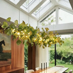A closer view of the Clérachic chandelier's linear green leaves, glowing warm beneath a sunroom skylight.