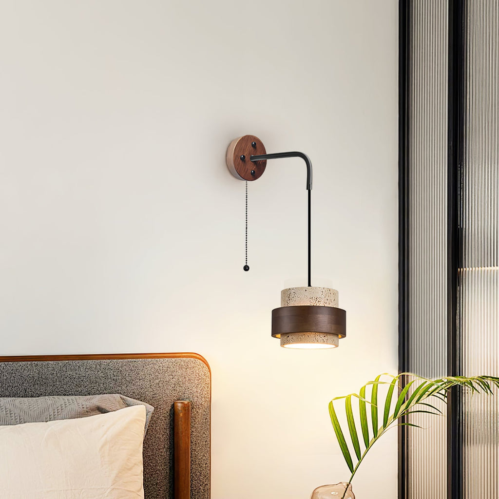 Pull-chain version of this Clérachic wall light on a white wall above a grey headboard, its shade lit warm underneath.