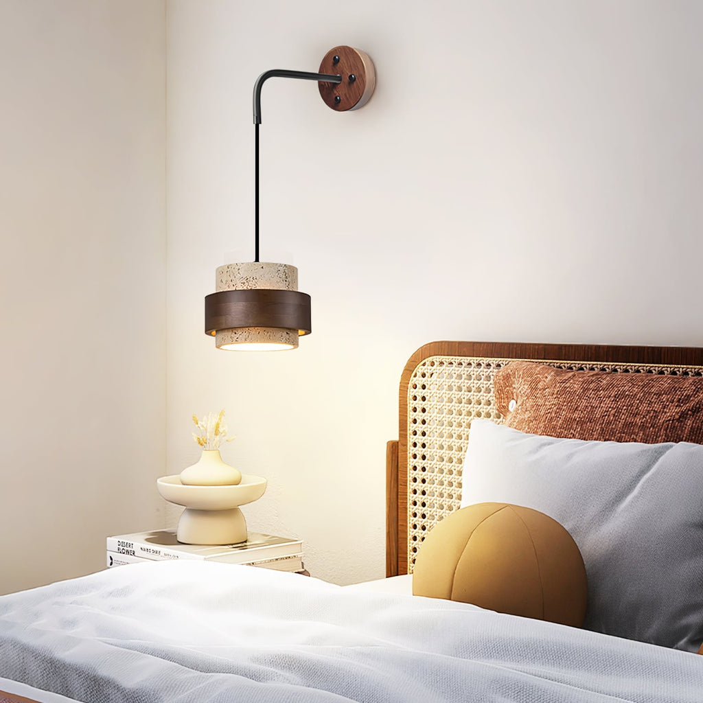 Beside a cane-backed bed with grey pillows and a mustard cushion, this Clérachic wall light glows over a nightstand holding a small vase.