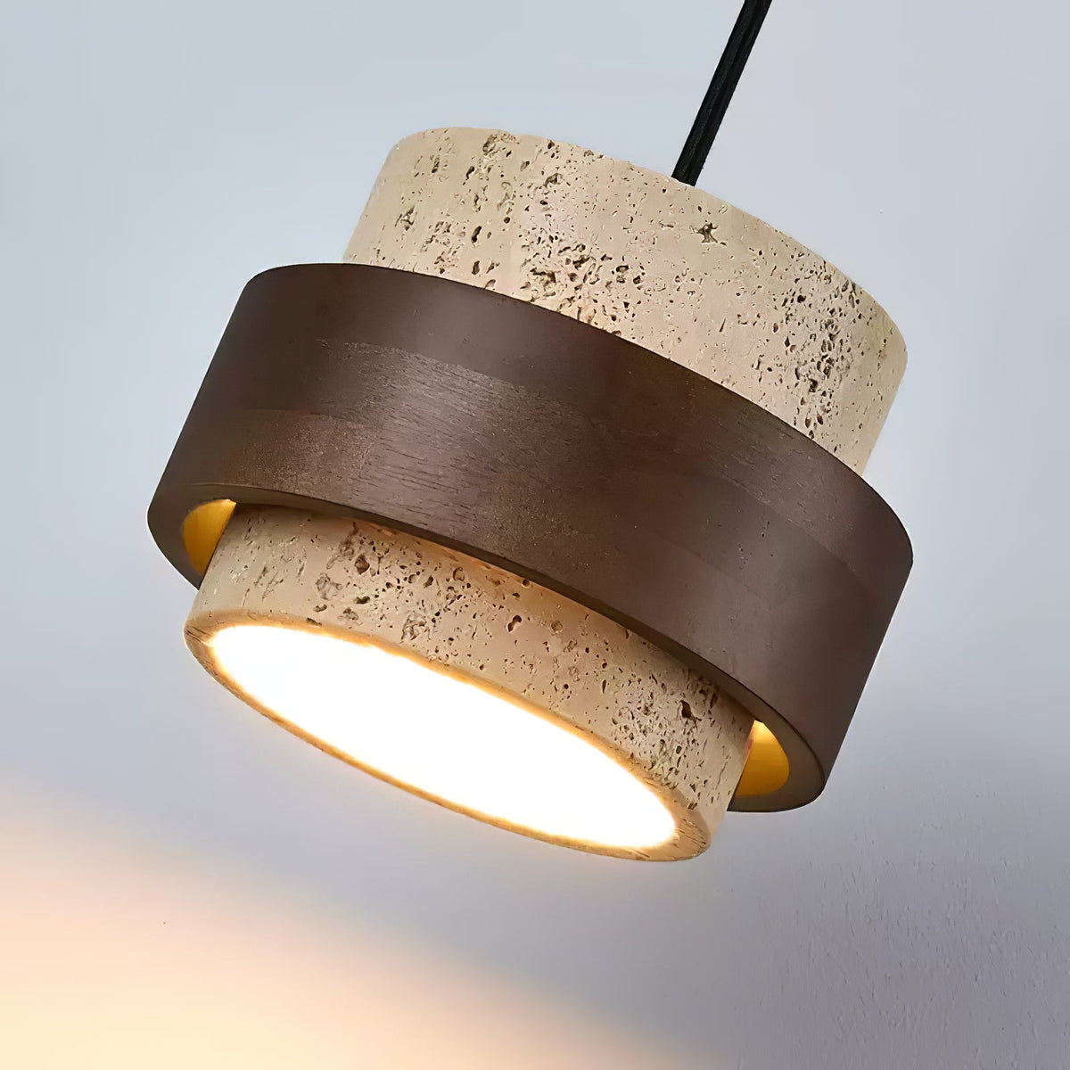 Angled close view of the pitted travertine and walnut band on this Clérachic wall light, with the frosted lit diffuser facing down.
