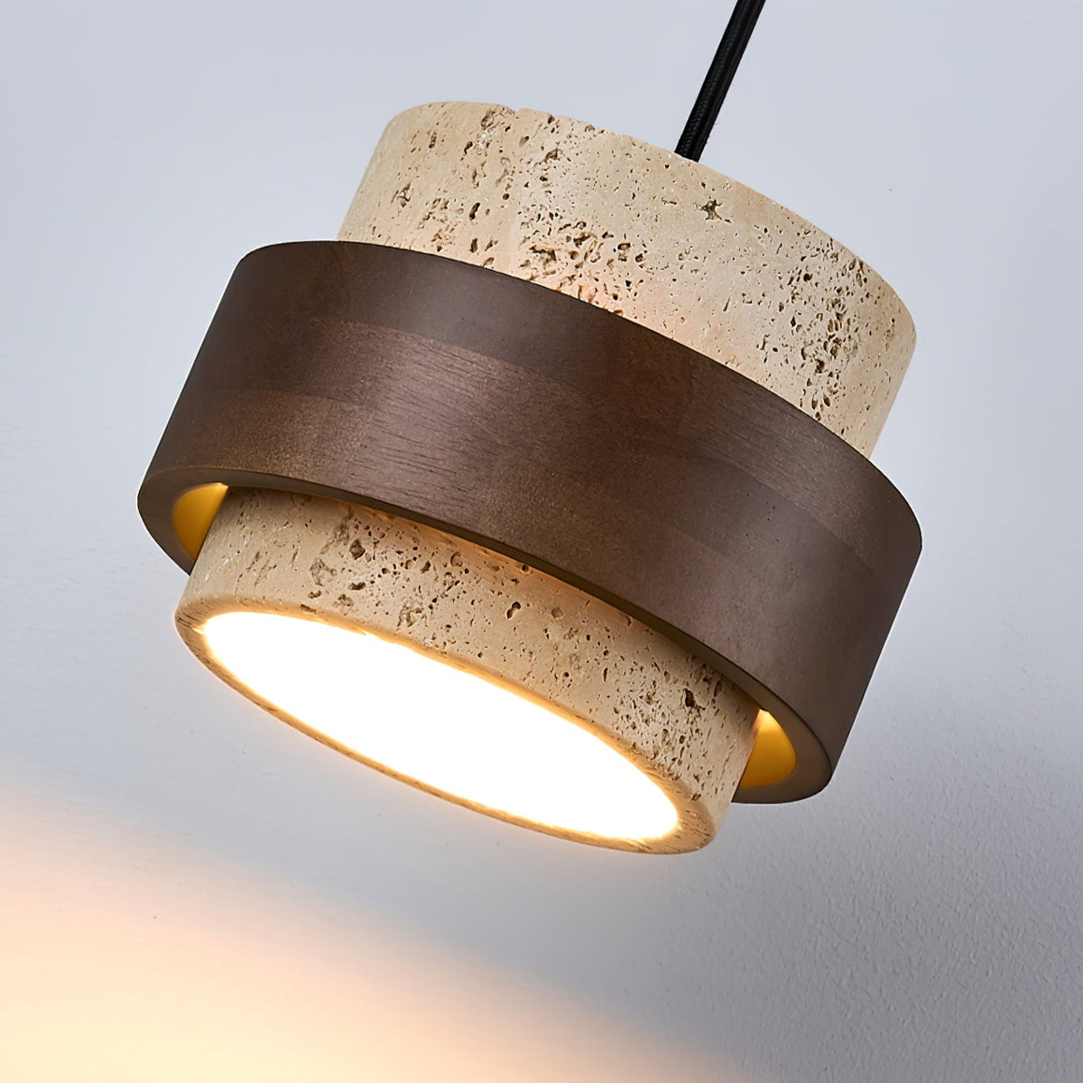 Tilted close view of the walnut ring wrapped around the travertine body of this Clérachic wall light, with its glowing base.