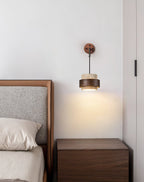 This Clérachic wall light lit beside a bed with a grey headboard, casting a warm glow over a dark walnut bedside table.