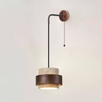 Pull-chain Clérachic wall light on a pale wall, its black arm reaching out from a walnut plate to a lit travertine and walnut shade.