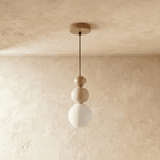 Clérachic pendant of a wood bead, a travertine bead and a white glass globe on a slim black cord, hung against limewash.
