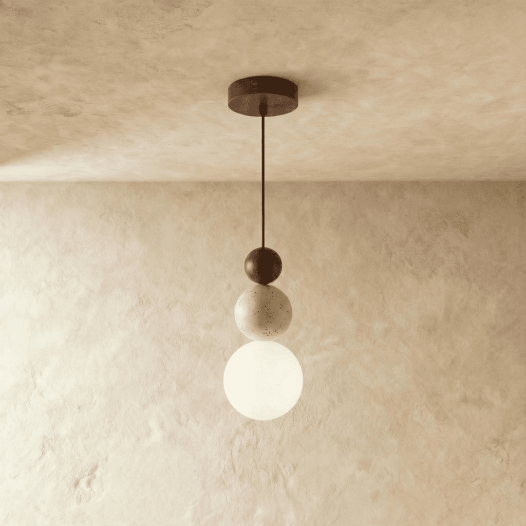 Clérachic stacked pendant with a dark walnut bead, travertine bead and white glass globe on a cord, against a limewashed wall.