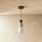 Clérachic walnut-toned stacked pendant with a travertine bead and a white glass globe, shown unlit against soft plaster.