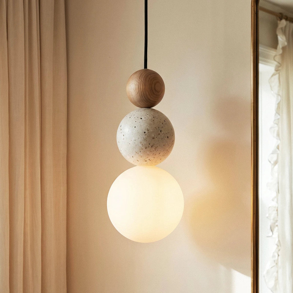 Close view of a Clérachic pendant: oak-grain wood bead, speckled travertine bead and a softly glowing white glass globe.