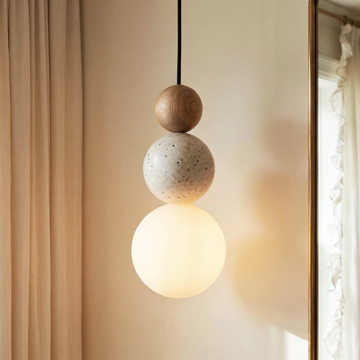 Close view of a Clérachic pendant: oak-grain wood bead, speckled travertine bead and a softly glowing white glass globe.