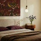 Clérachic pendant with a dark wood bead, travertine bead and glowing globe, hung beside a bed with a round walnut bedside table.