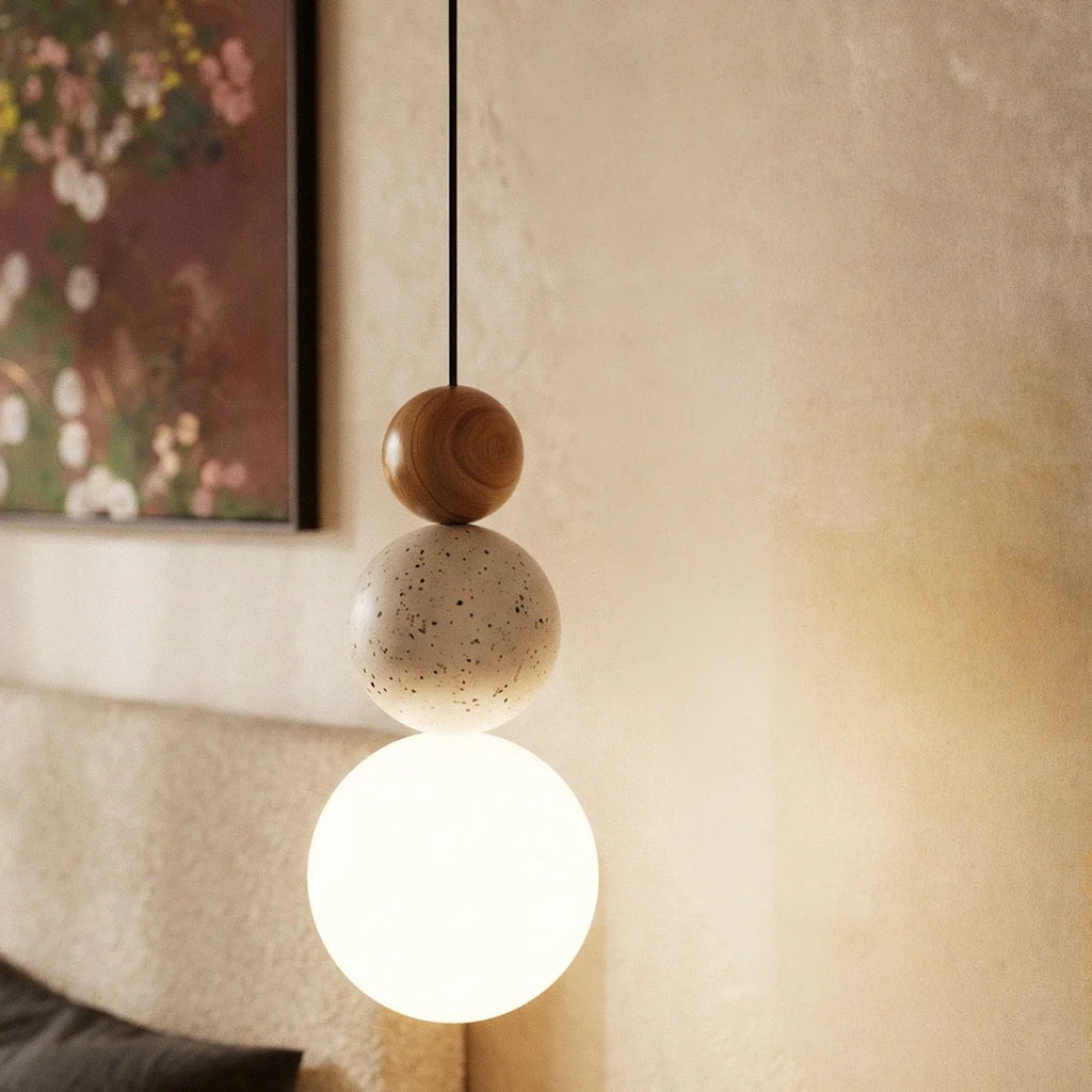 Close view of a Clérachic pendant with a warm wood bead, pitted travertine bead and a bright white glass globe on a black cord.