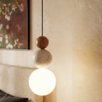 Close view of a Clérachic pendant with a warm wood bead, pitted travertine bead and a bright white glass globe on a black cord.
