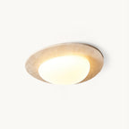 This Clérachic ceiling light on a plain white backdrop, with a pale travertine rim around a lit, rounded white glass shade.