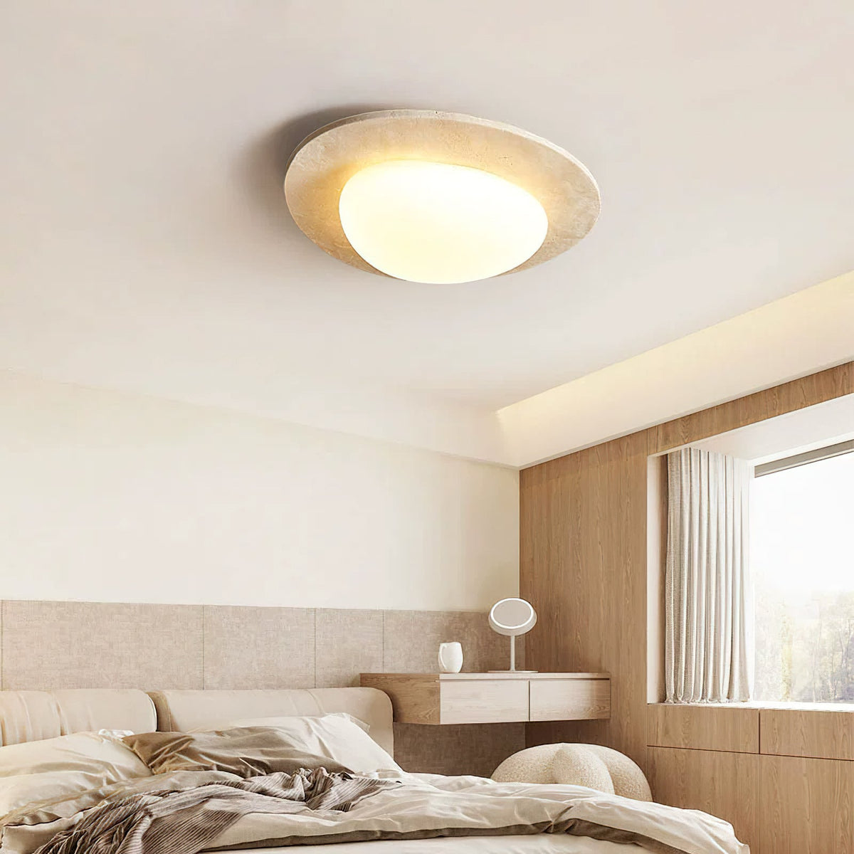 Flush-mounted Clérachic ceiling light glowing above a bedroom with a pale linen bed, a wooden wall panel and a window with sheer curtains.
