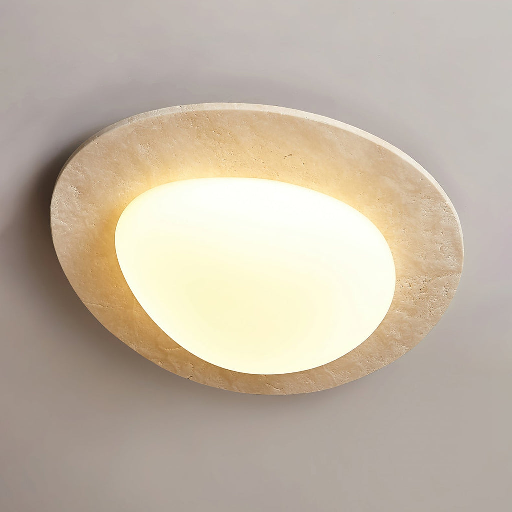 Angled view of this Clérachic ceiling light, showing the pitted surface of the travertine rim and the glowing white glass shade.