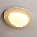 Angled view of this Clérachic ceiling light, showing the pitted surface of the travertine rim and the glowing white glass shade.