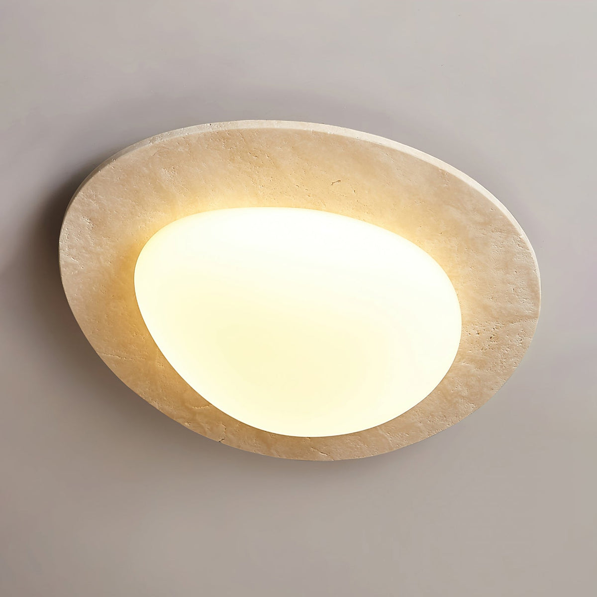 Angled view of this Clérachic ceiling light, showing the pitted surface of the travertine rim and the glowing white glass shade.