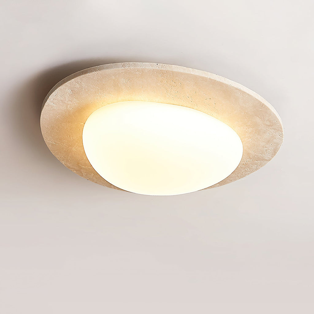 Lit Clérachic flush ceiling light from the side, its pebble-shaped glass shade glowing warm inside a pale stone rim.