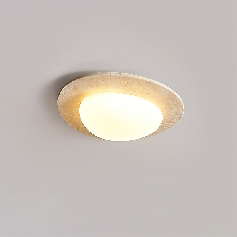 Smaller Clérachic ceiling light on a grey ceiling, its rounded glass shade lit warm inside a thin travertine rim.