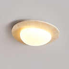 Larger-looking Clérachic ceiling light glowing against a grey ceiling, with a wide travertine rim around a rounded white shade.