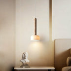 Lit beside a cream bed headboard, this Clérachic pendant light glows warmly above a bedside shelf with a small white bust.