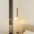 This Clérachic pendant light hangs at a bedside beside a reeded glass panel, its white dome glowing a soft warm yellow.
