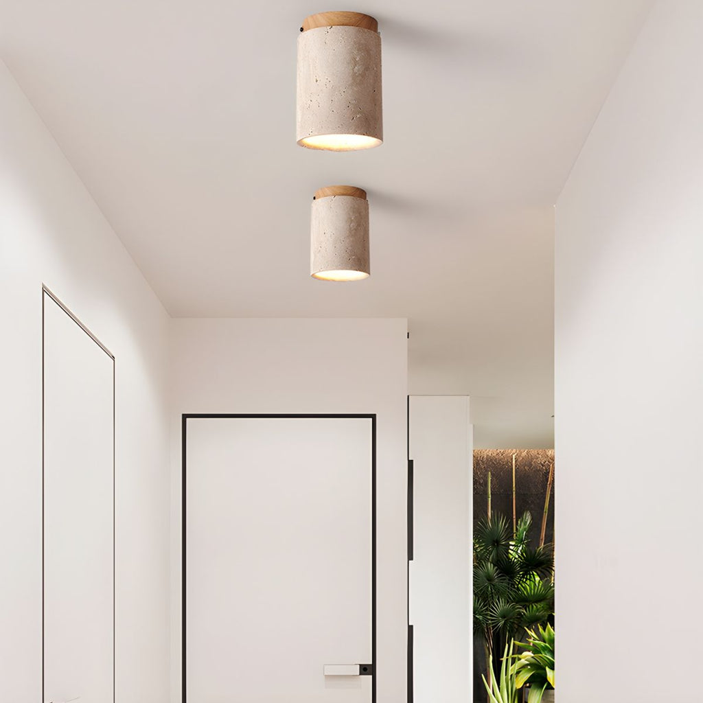 Two Clérachic travertine ceiling lights lit in a white hallway, one behind the other above a slim black-framed door.