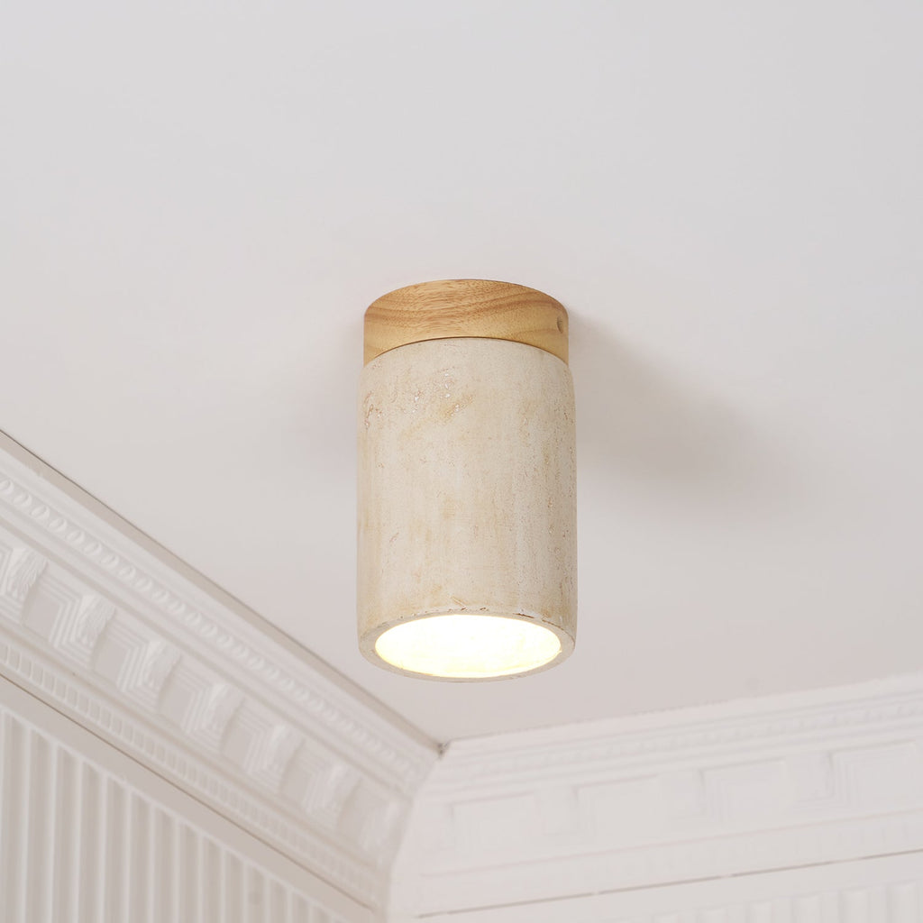 Slim Clérachic travertine cylinder with a wood-colour cap, its base glowing softly against a white ceiling corner with moulding.