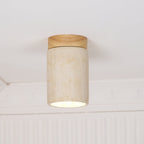 Front view of a Clérachic ceiling light, a cream travertine cylinder under a wood cap, with the glow showing at the rim.