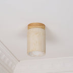 Clérachic travertine ceiling light switched off, the wood cap and stone shade clear against white cornice moulding.