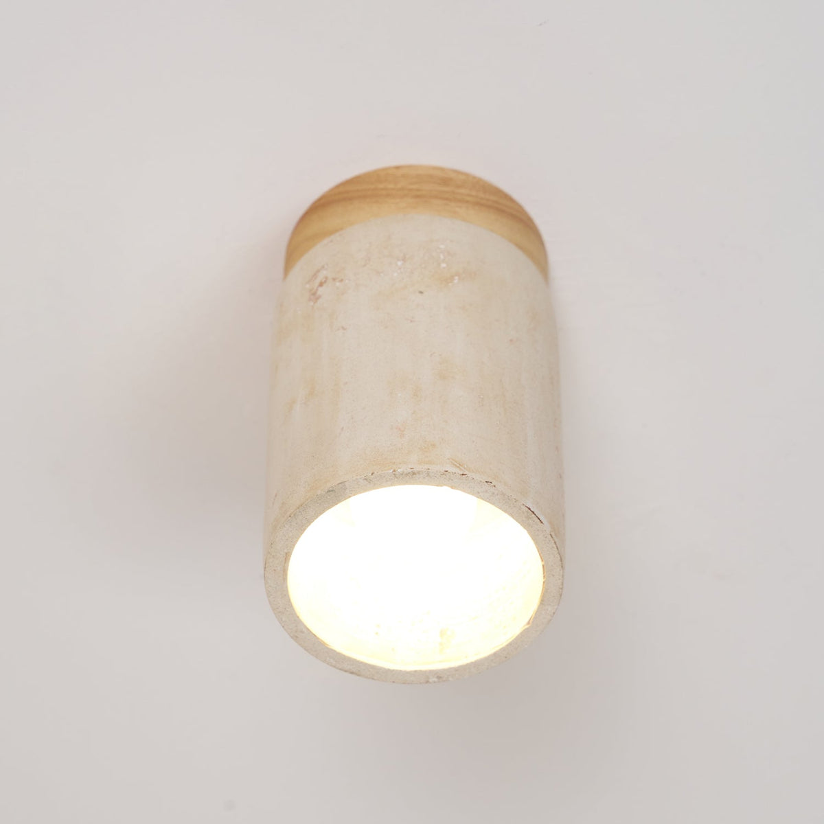 Close view of the lit open end of this Clérachic travertine ceiling light, its wood cap just visible above the stone.