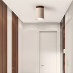 Single Clérachic ceiling light with a walnut cap lit above a white hallway with slatted wood walls and a closed door.