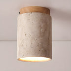 Clérachic ceiling light with a wood-colour cap, the porous travertine surface showing its natural pitting above a lit rim.
