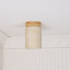 Clérachic travertine cylinder with a wood cap, unlit against a white ceiling and panelled cornice, the inner stone visible.
