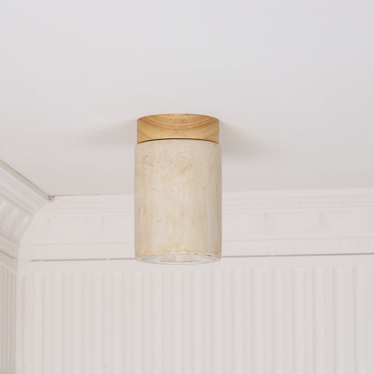 Clérachic travertine cylinder with a wood cap, unlit against a white ceiling and panelled cornice, the inner stone visible.