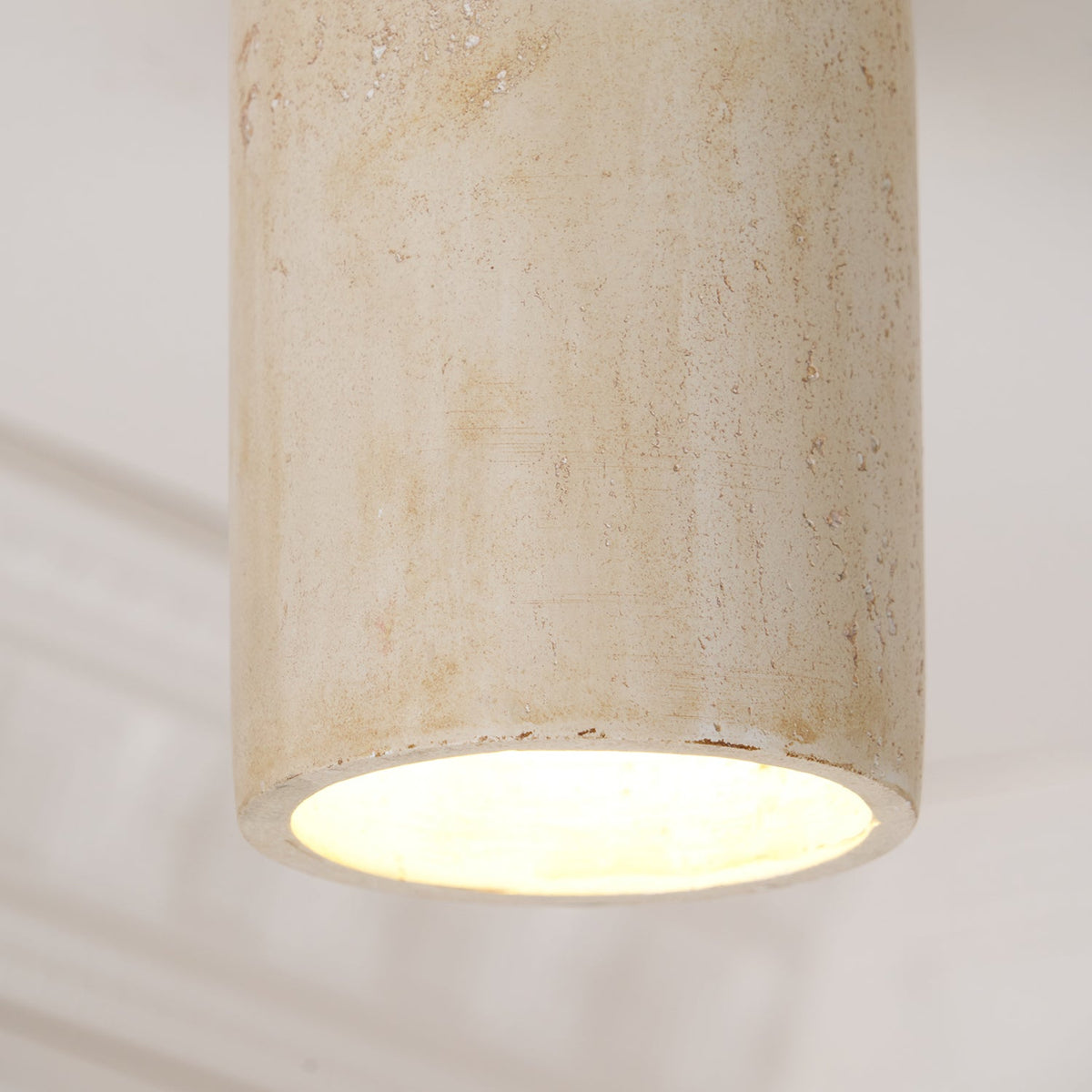 Close view of the yellow-toned travertine cylinder on this Clérachic ceiling light, its lit base casting a warm glow.