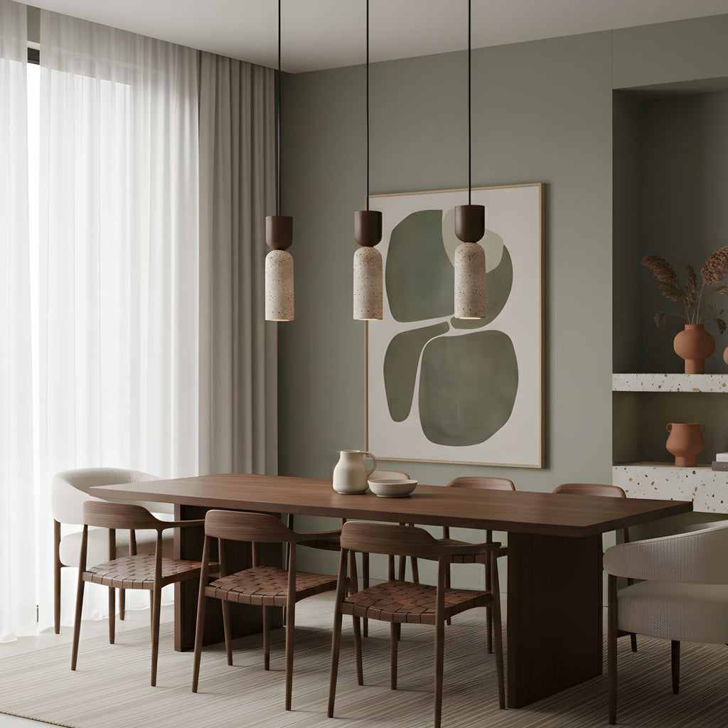Three Clérachic travertine pendants hang over a walnut dining table, with a sage-green wall and abstract artwork behind.