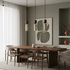 Three Clérachic travertine pendants hang over a walnut dining table, with a sage-green wall and abstract artwork behind.