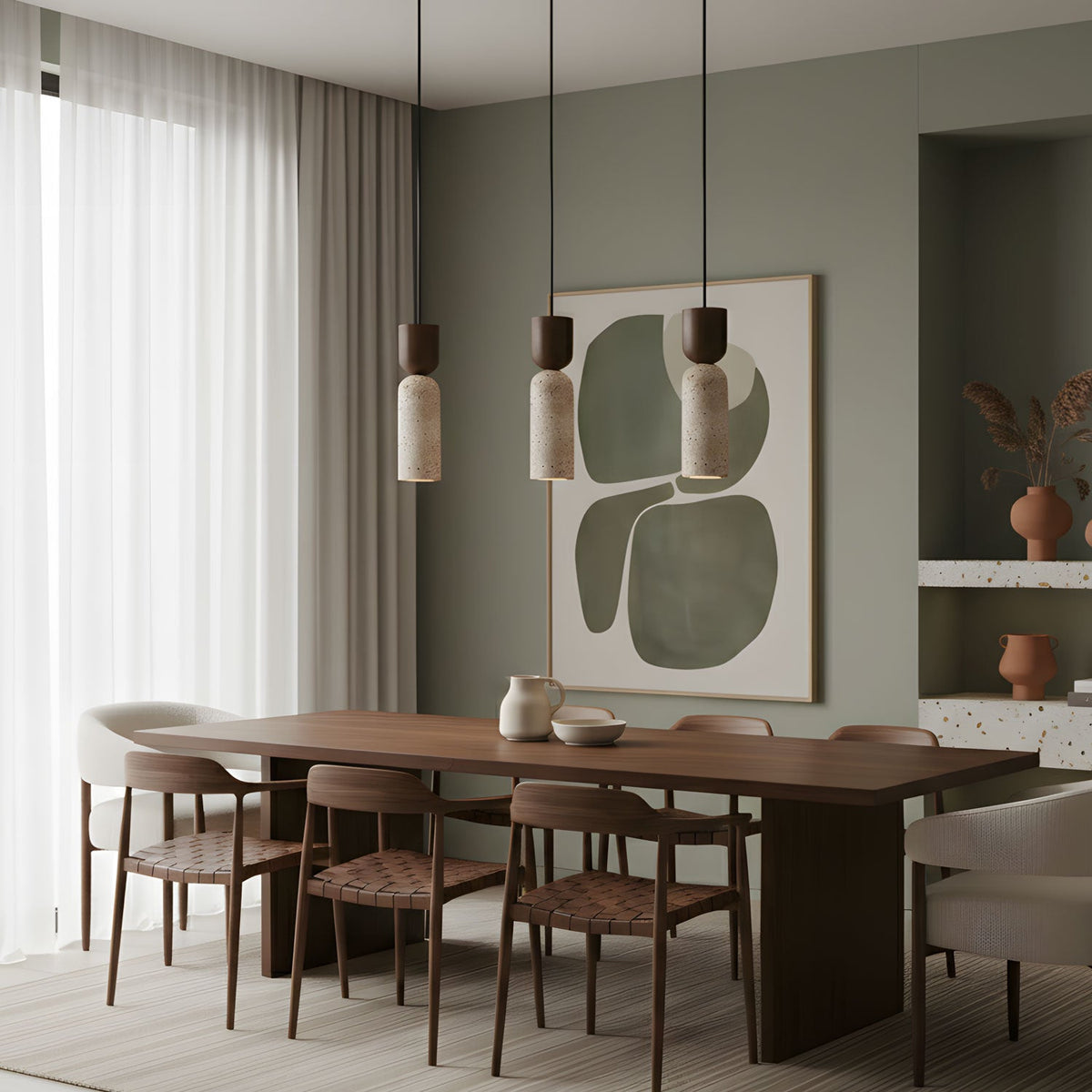 Three Clérachic travertine pendants hang over a walnut dining table, with a sage-green wall and abstract artwork behind.