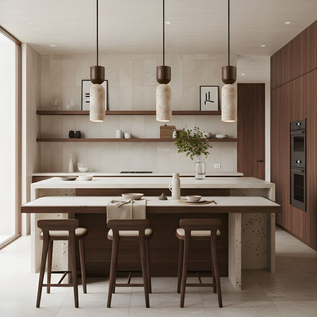 A row of three Clérachic stone pendants above a pale kitchen island, with walnut stools and open wooden shelves beyond.