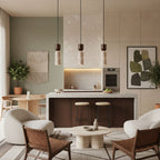 Clérachic travertine pendants lit above a kitchen island in an open living space with cream armchairs and a sage-green wall.