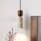 Single Clérachic pendant with a walnut cap and porous travertine body, glowing warm beside a wooden headboard and red berry stems.