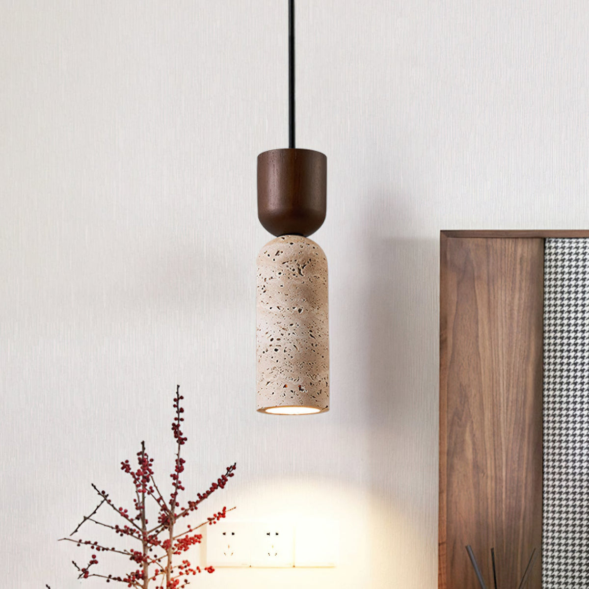 Single Clérachic pendant with a walnut cap and porous travertine body, glowing warm beside a wooden headboard and red berry stems.