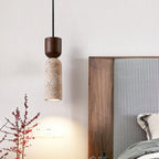 Bedside view of a Clérachic travertine pendant with a walnut cap, casting a soft pool of warm light on the wall.