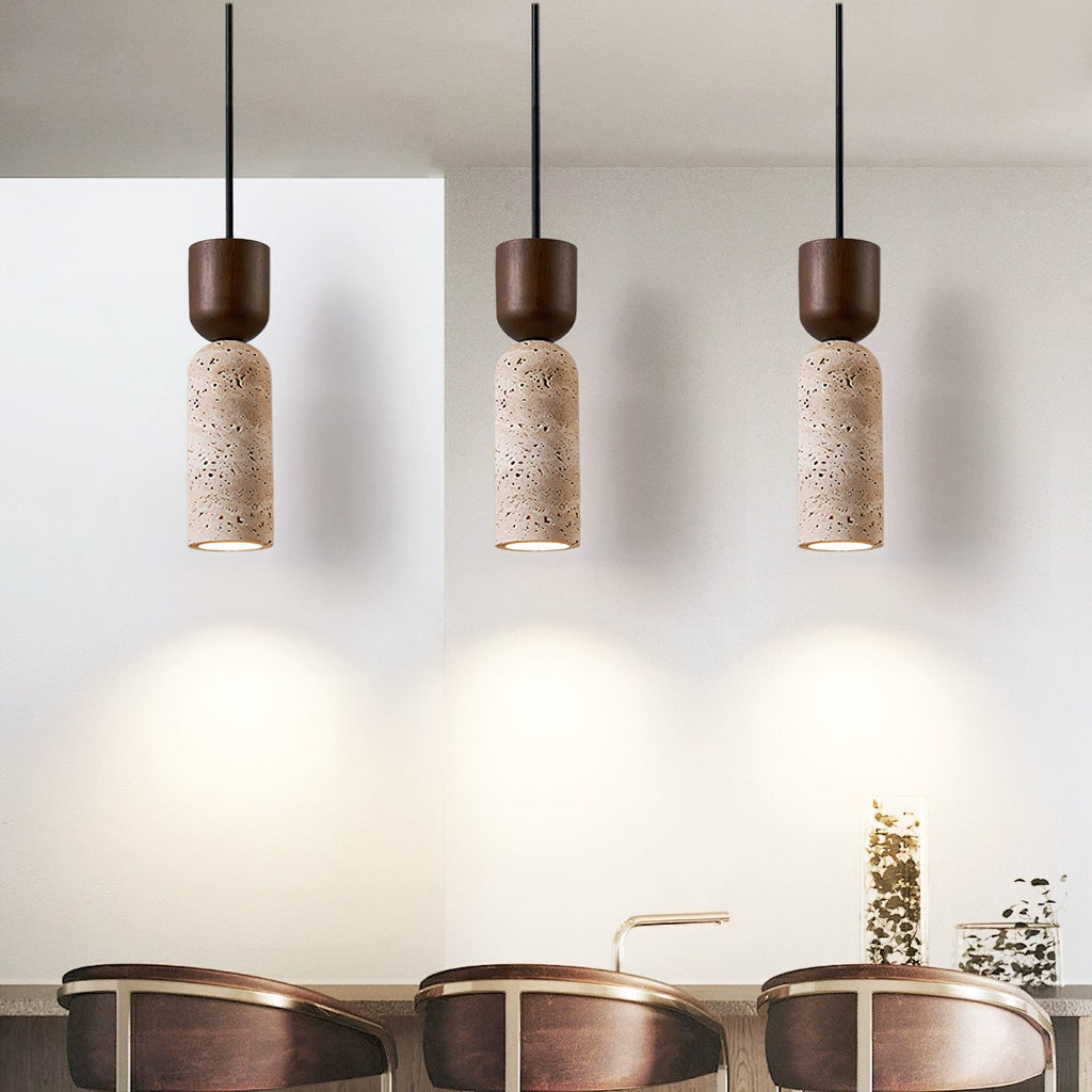 Three lit Clérachic travertine pendants side by side, each throwing a cone of warm light onto a pale wall above dining chairs.