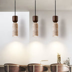 Three lit Clérachic travertine pendants side by side, each throwing a cone of warm light onto a pale wall above dining chairs.