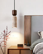 Clérachic travertine pendant hanging beside a bed, with a walnut headboard, a nightstand and a bare red-berried branch nearby.