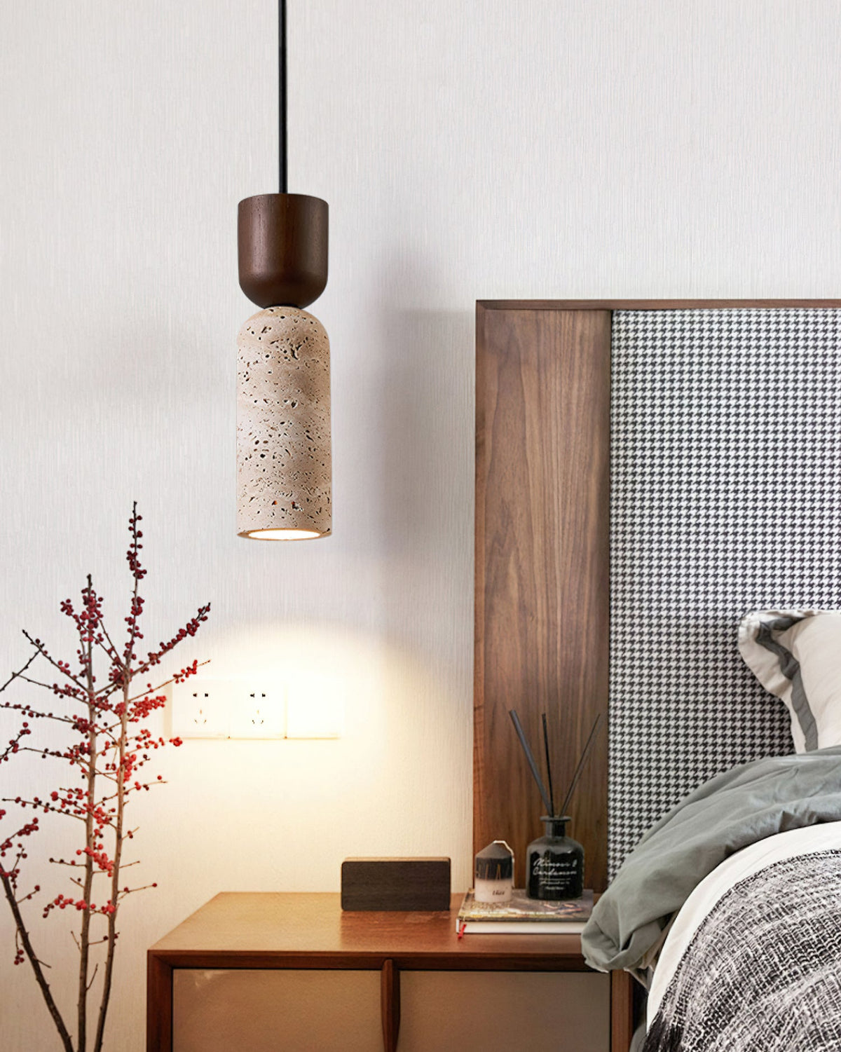 Clérachic travertine pendant hanging beside a bed, with a walnut headboard, a nightstand and a bare red-berried branch nearby.
