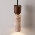 Clérachic pendant with a walnut cap above a beige travertine cylinder, its light pooling softly on the surface below.