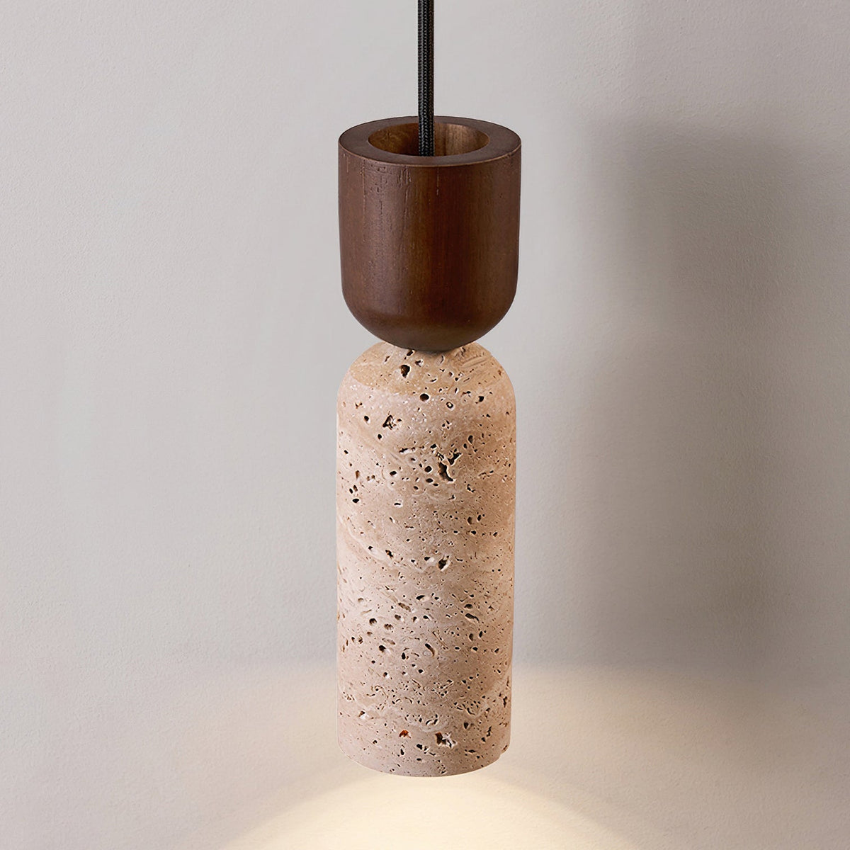 Clérachic pendant with a walnut cap above a beige travertine cylinder, its light pooling softly on the surface below.